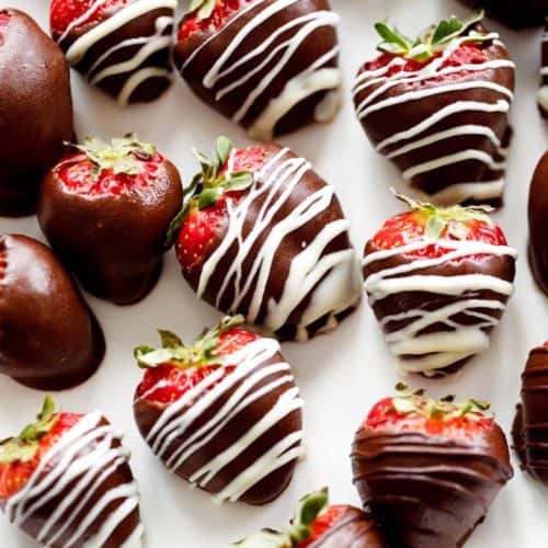 A white plate full of alcohol infused Strawberries Covered in Chocolate . A rose sits behind the plate for romantic decoration.