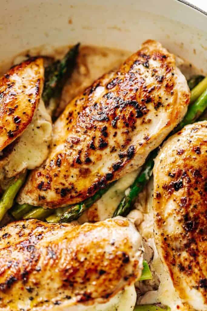An overhead image of four asparagus and mozzarella cheese stuffed chicken breasts in a white casserole dish.