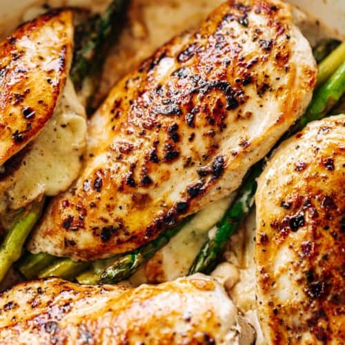 An overhead image of four asparagus and mozzarella cheese stuffed chicken breasts in a white casserole dish.