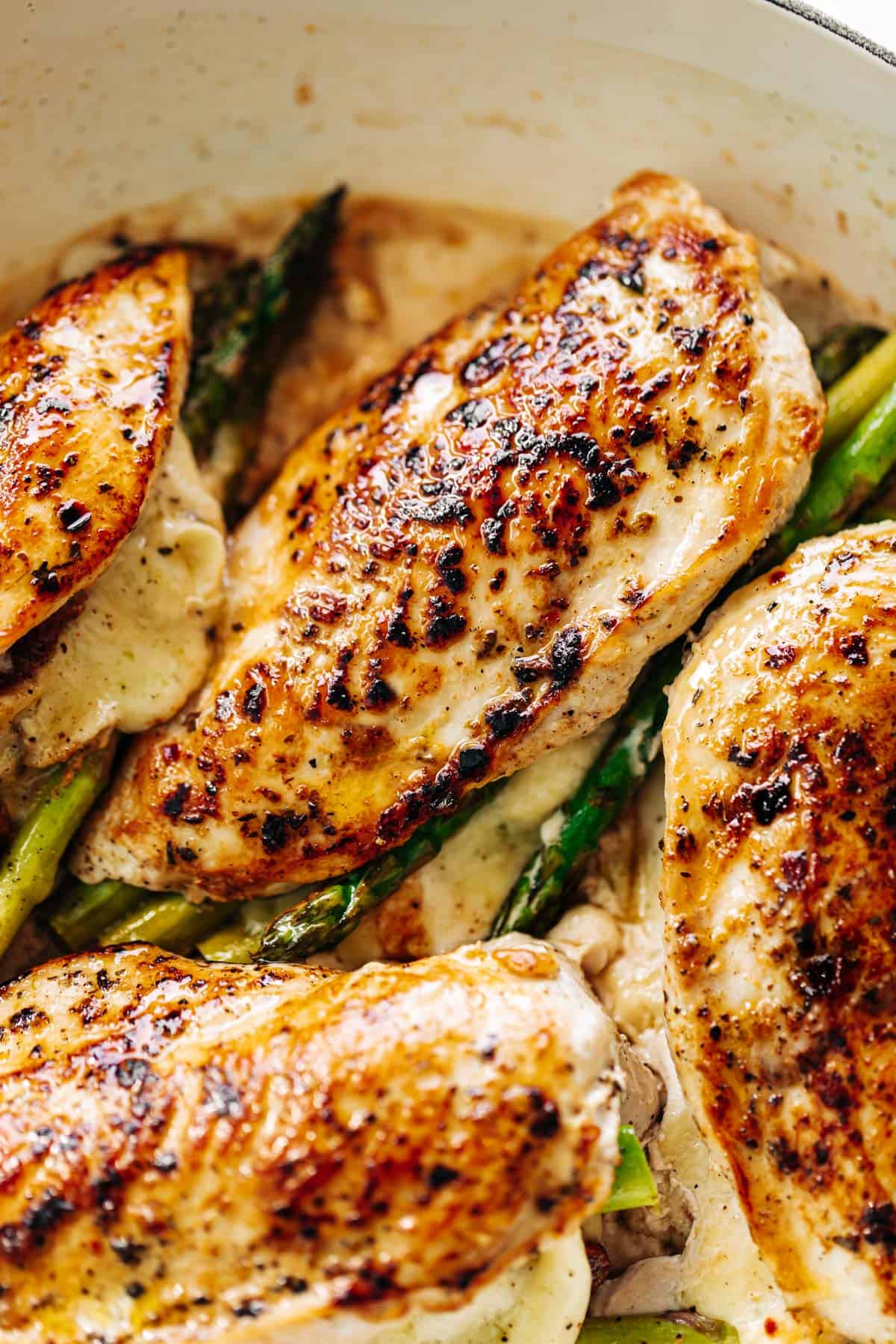 An overhead image of four asparagus and mozzarella cheese stuffed chicken breasts in a white casserole dish | cafedelites.com