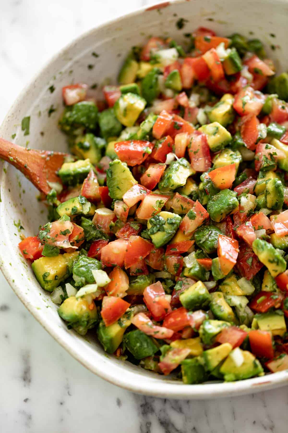 A bowl of avocado salsa being mixed with a wooden spoon.