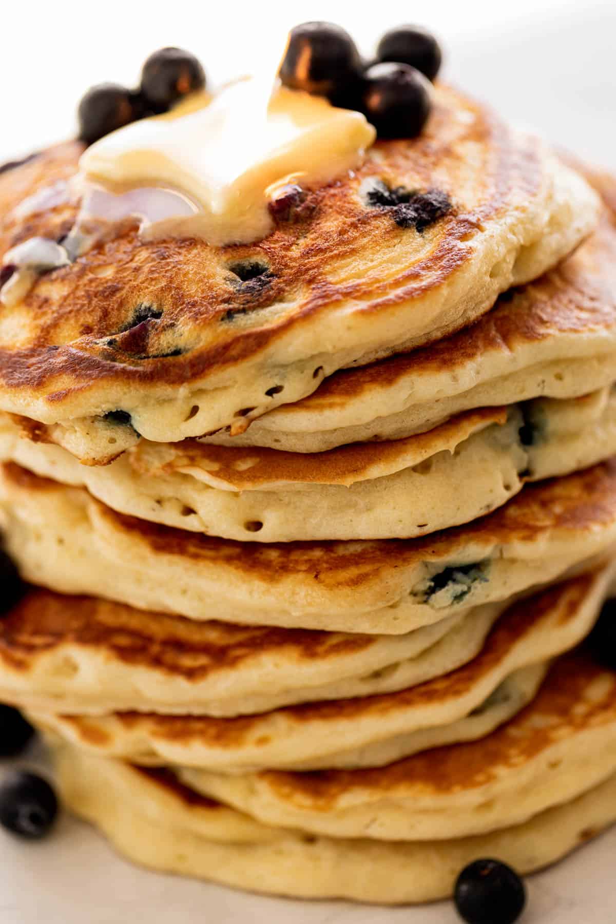 A stack of Blueberry Pancakes on a plate topped with fresh blueberries and melted butter.