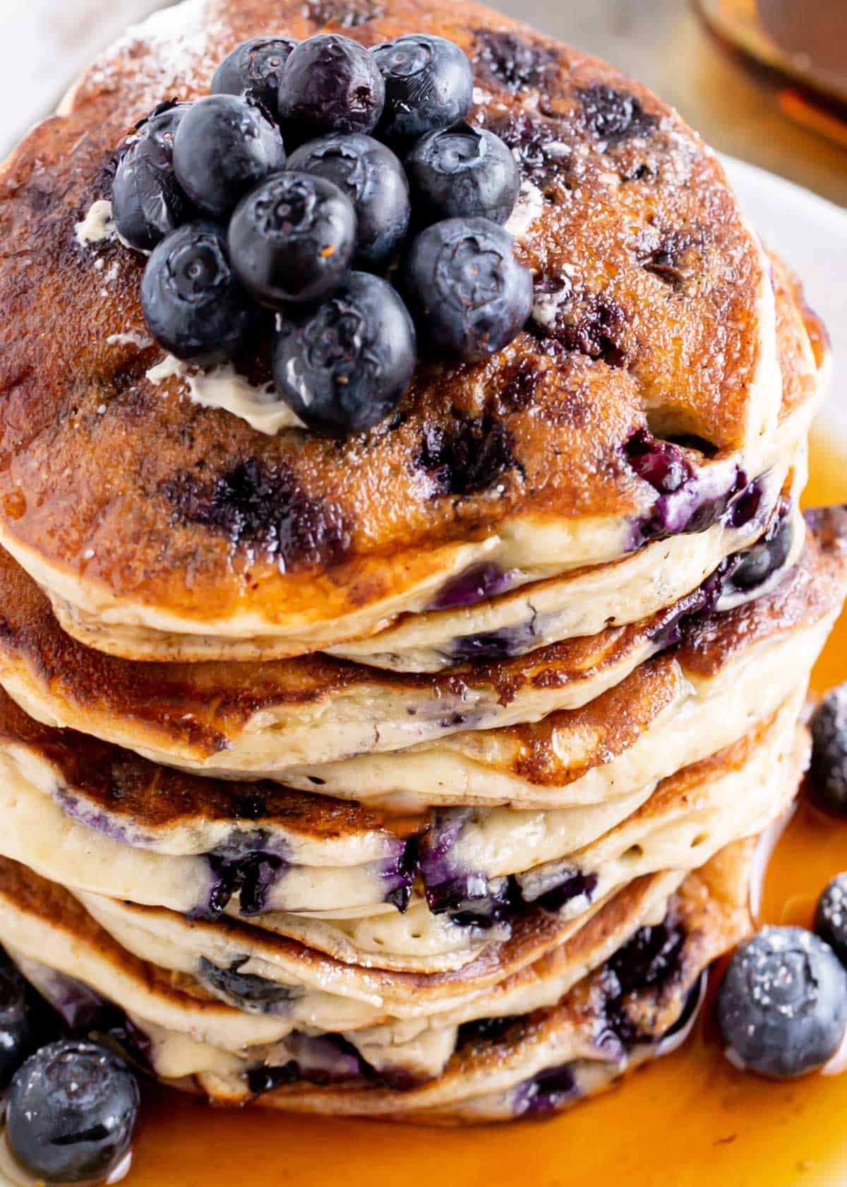 A stack of Blueberry Ricotta Pancakes on a plate with maple syrup. Topped with fresh blueberries | cafedelites.com