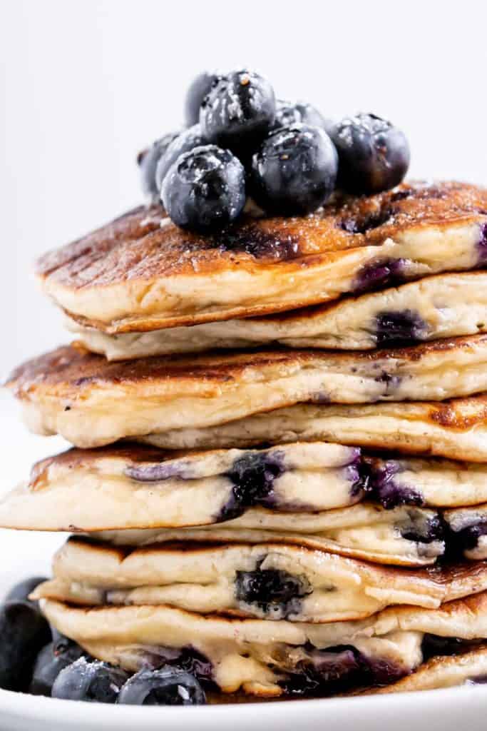 A stack of Blueberry Pancakes on a plate with maple syrup. Topped with fresh blueberries | cafedelites.com