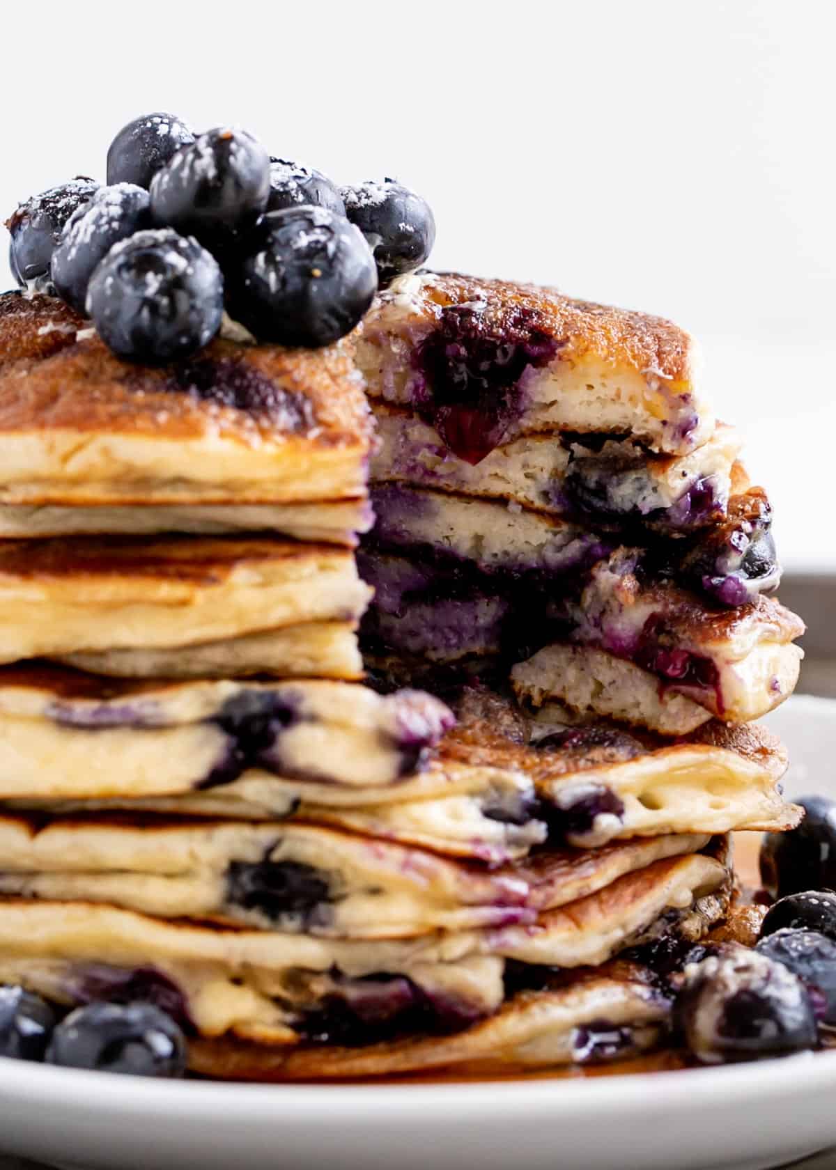 Cutting into a stack of Blueberry Ricotta Pancakes on a plate with maple syrup. Topped with fresh blueberries | cafedelites.com