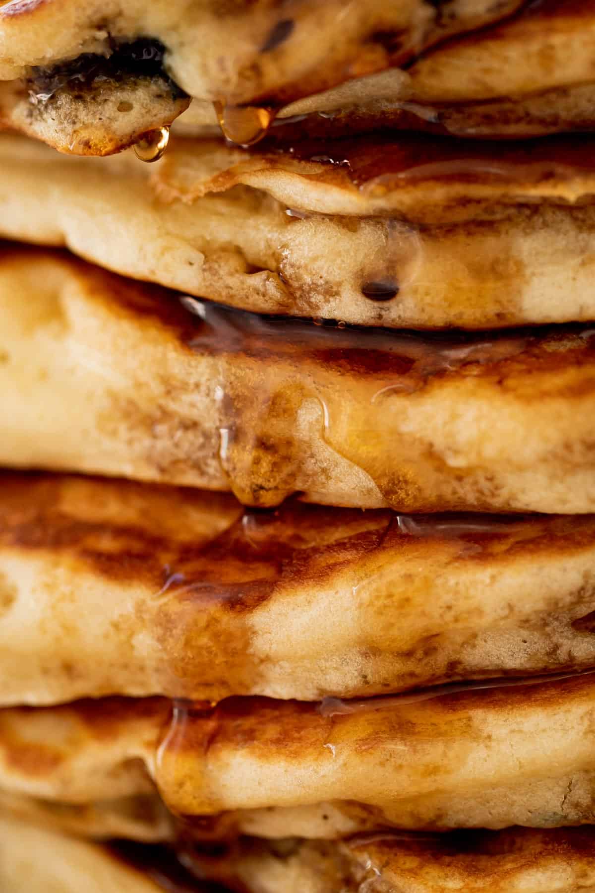 A close up stack of Blueberry Pancakes on a plate with maple syrup.