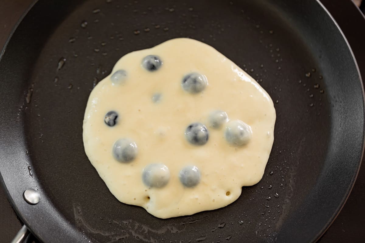 Cooking blueberry pancakes in a black nonstick pan.