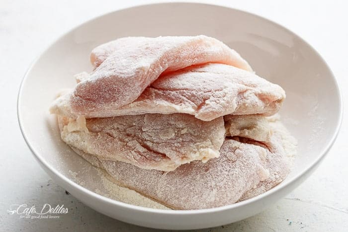 Four chicken breasts dredged in flour in a bowl