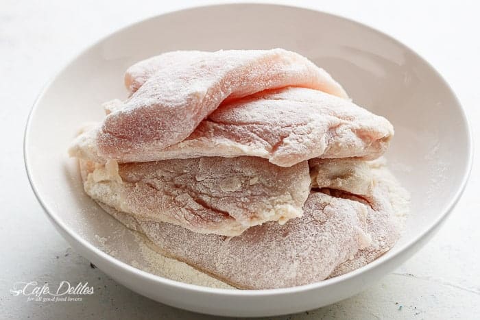 Four chicken breasts dredged in flour in a bowl.