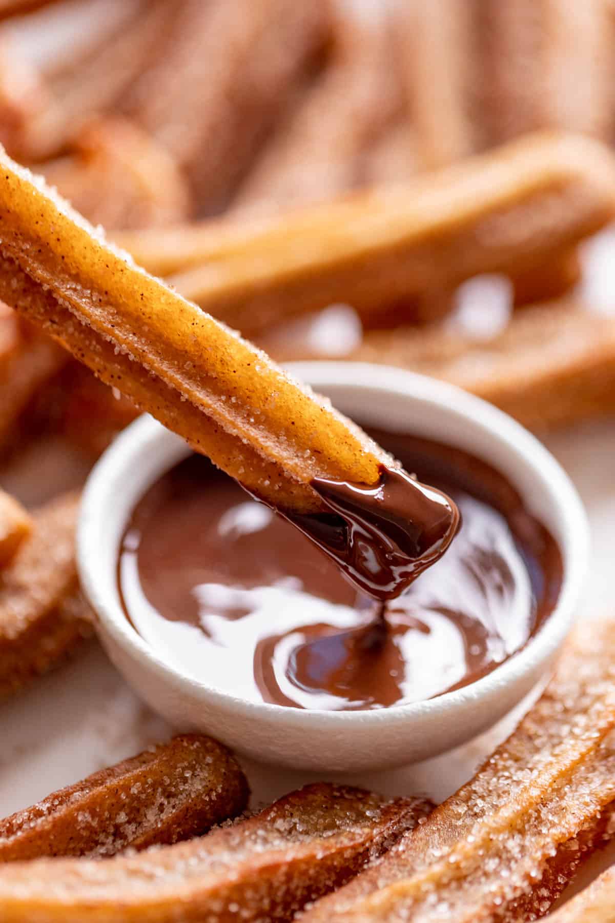 A close up dipping churros into a bowl of melted chocolate | cafedelites.com
