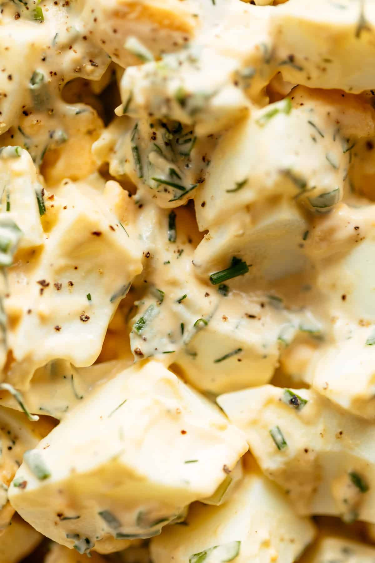 A close up image of egg salad, with creamy mayo and chives mixed through it.