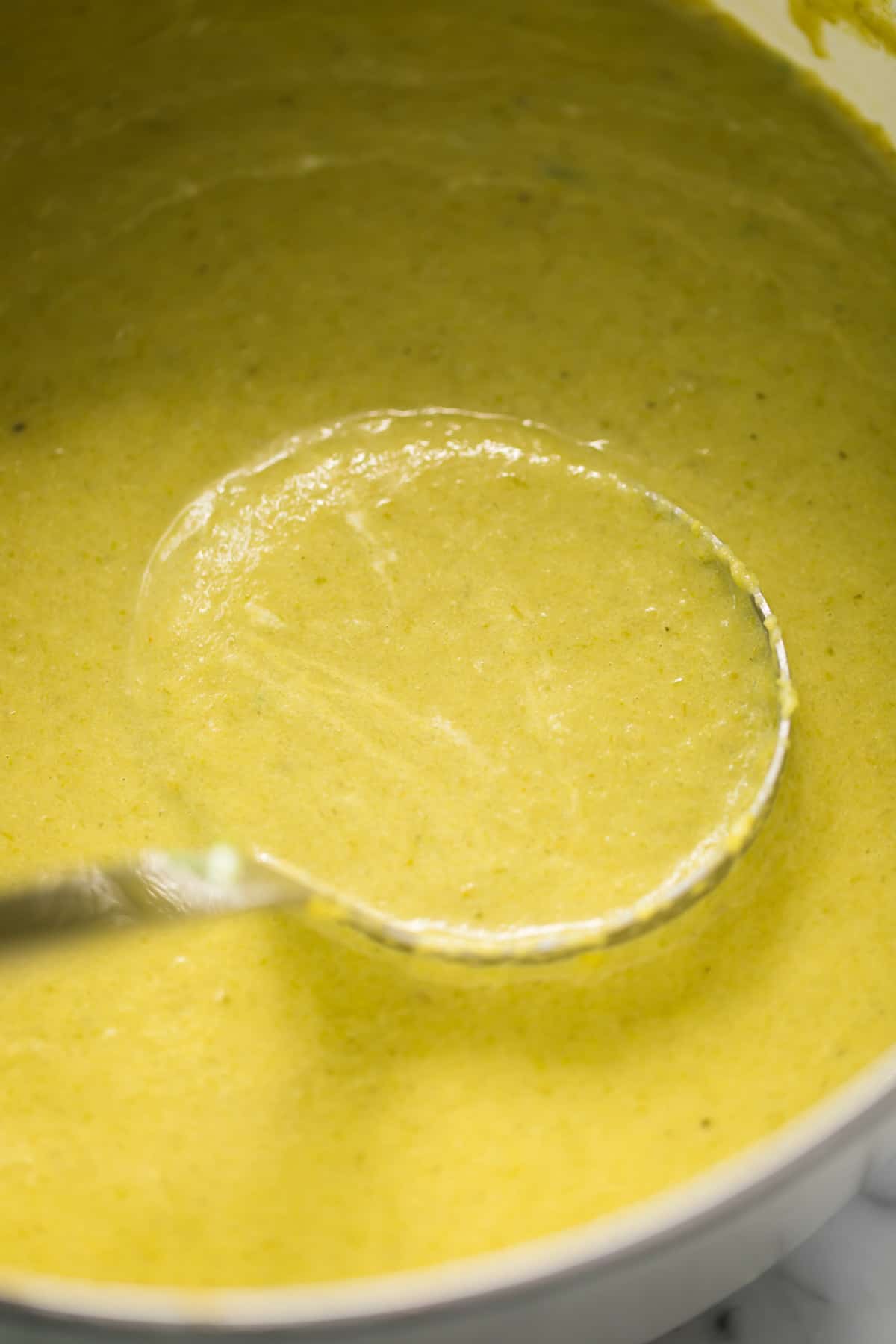 Smooth asparagus soup just blended and poured back into the pot to continue simmering. A silver ladle stirs through the soup.