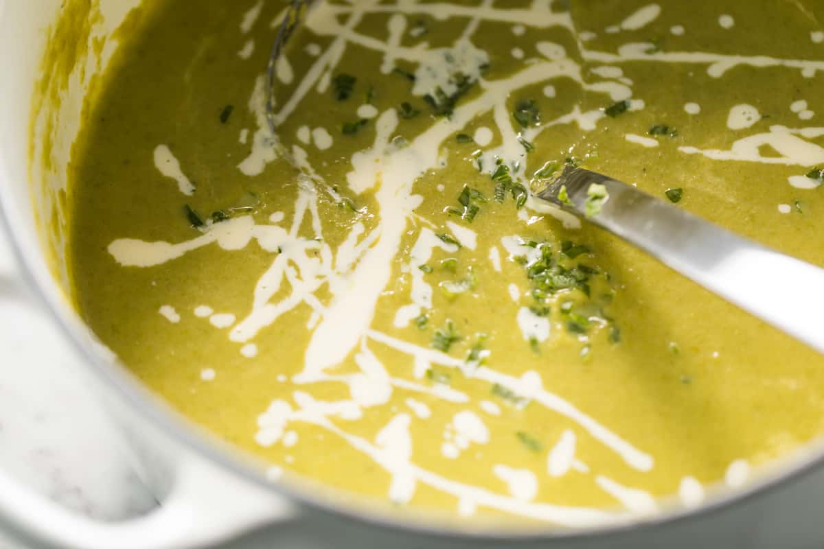 A white heavy based pot full of creamy asparagus soup! Garnished with fresh chopped chives and a little extra cream on top.