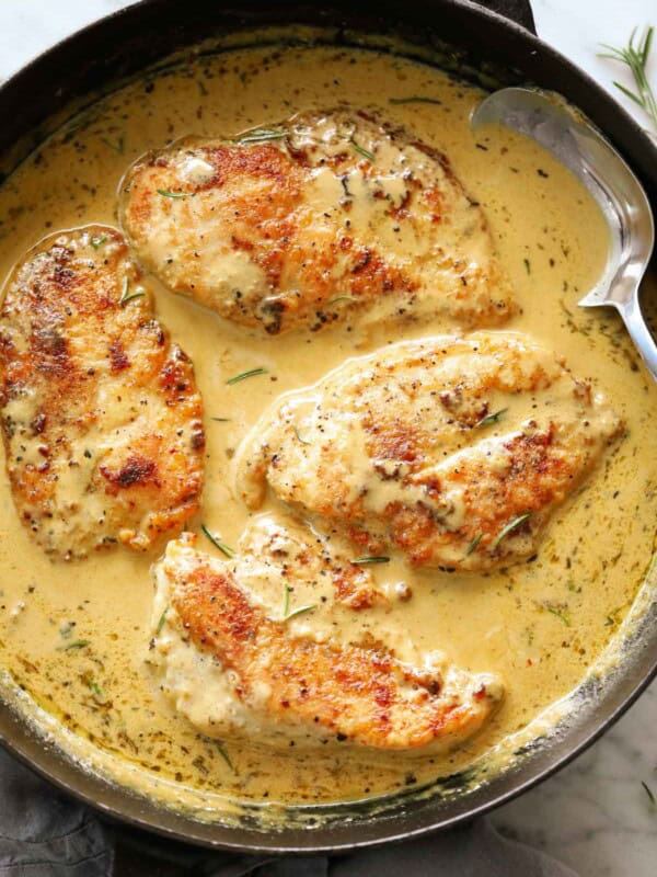 Creamy mustard chicken breasts in a black Staub skillet with a metal spoon.