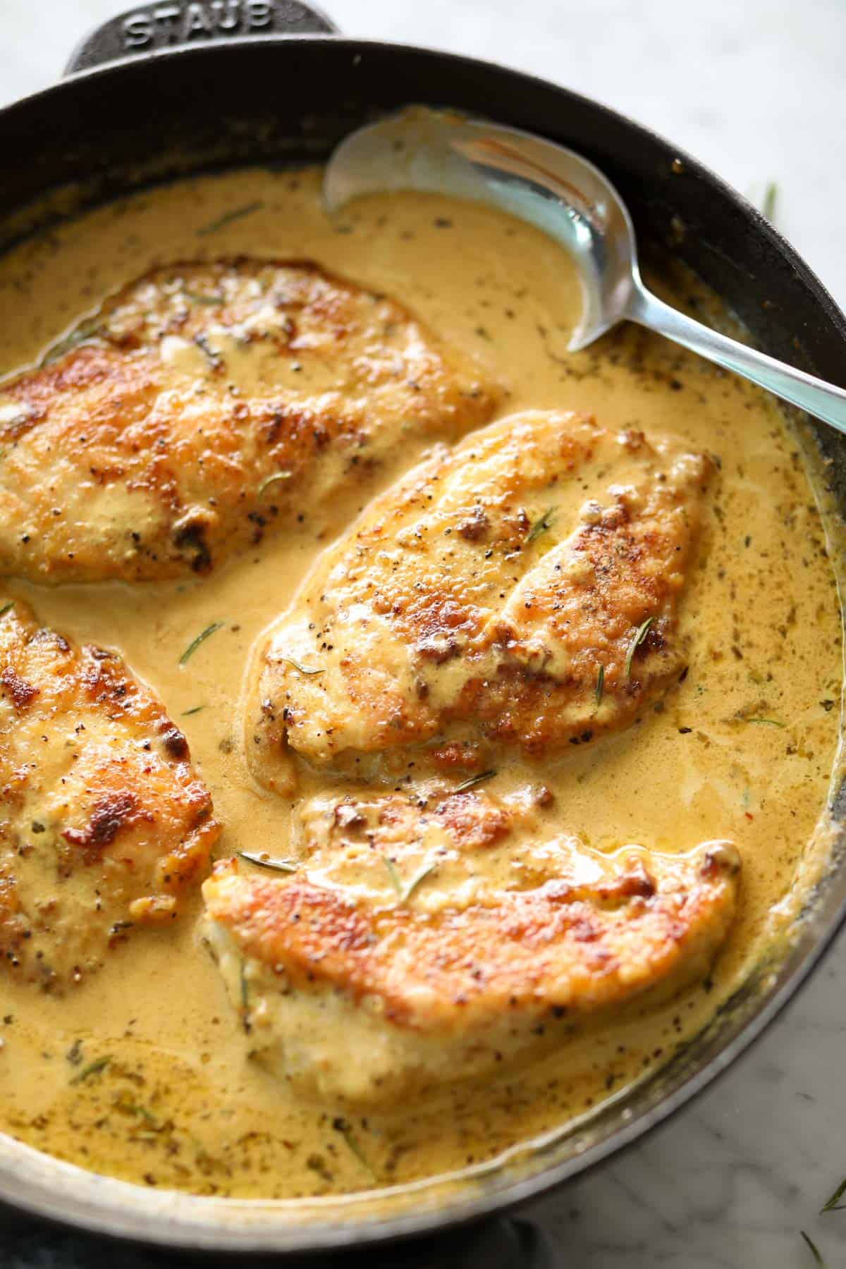 Creamy mustard chicken breasts in a black Staub skillet with a metal spoon | cafedelites.com