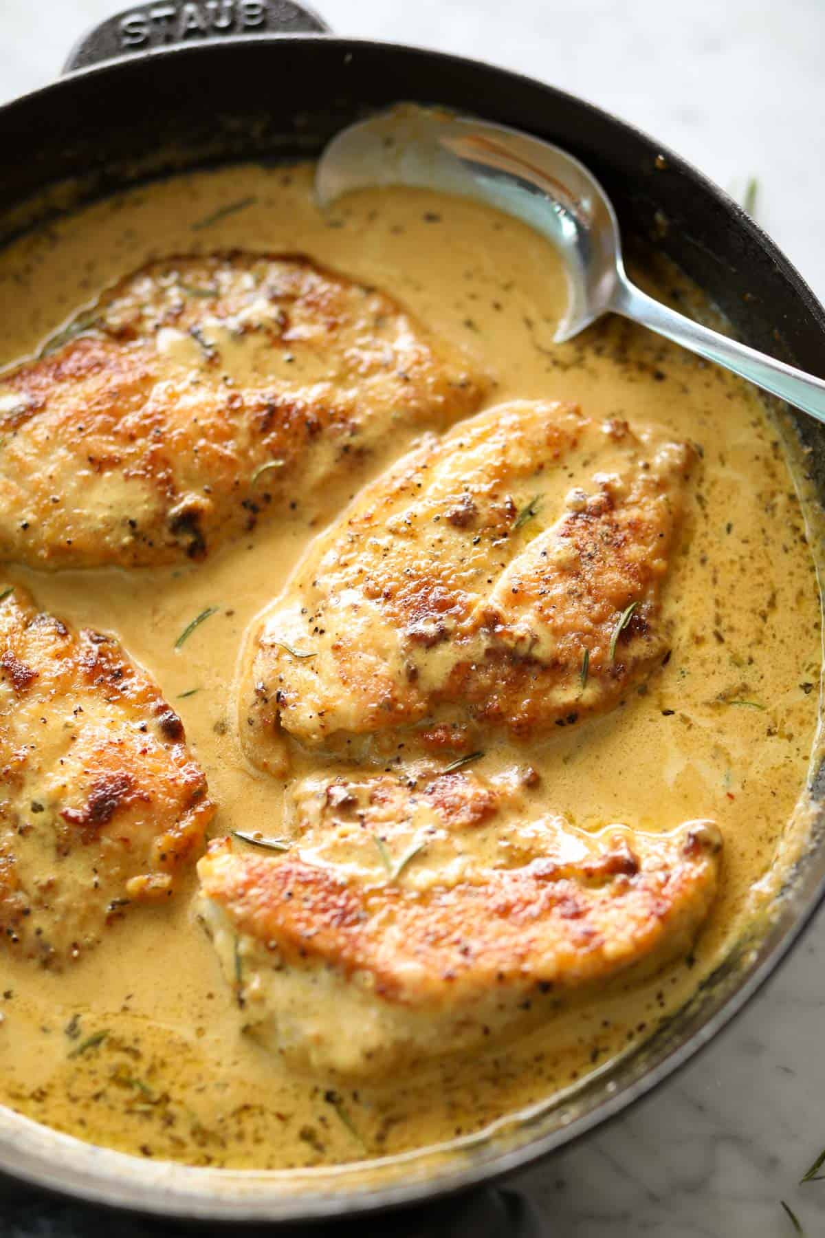 Creamy mustard chicken breasts in a black Staub skillet with a metal spoon.