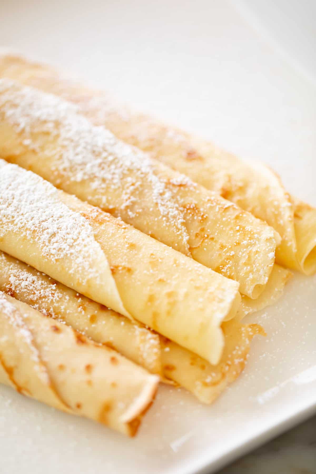 Rolled up crepes on a plate with confectioners sugar | cafedelites.com