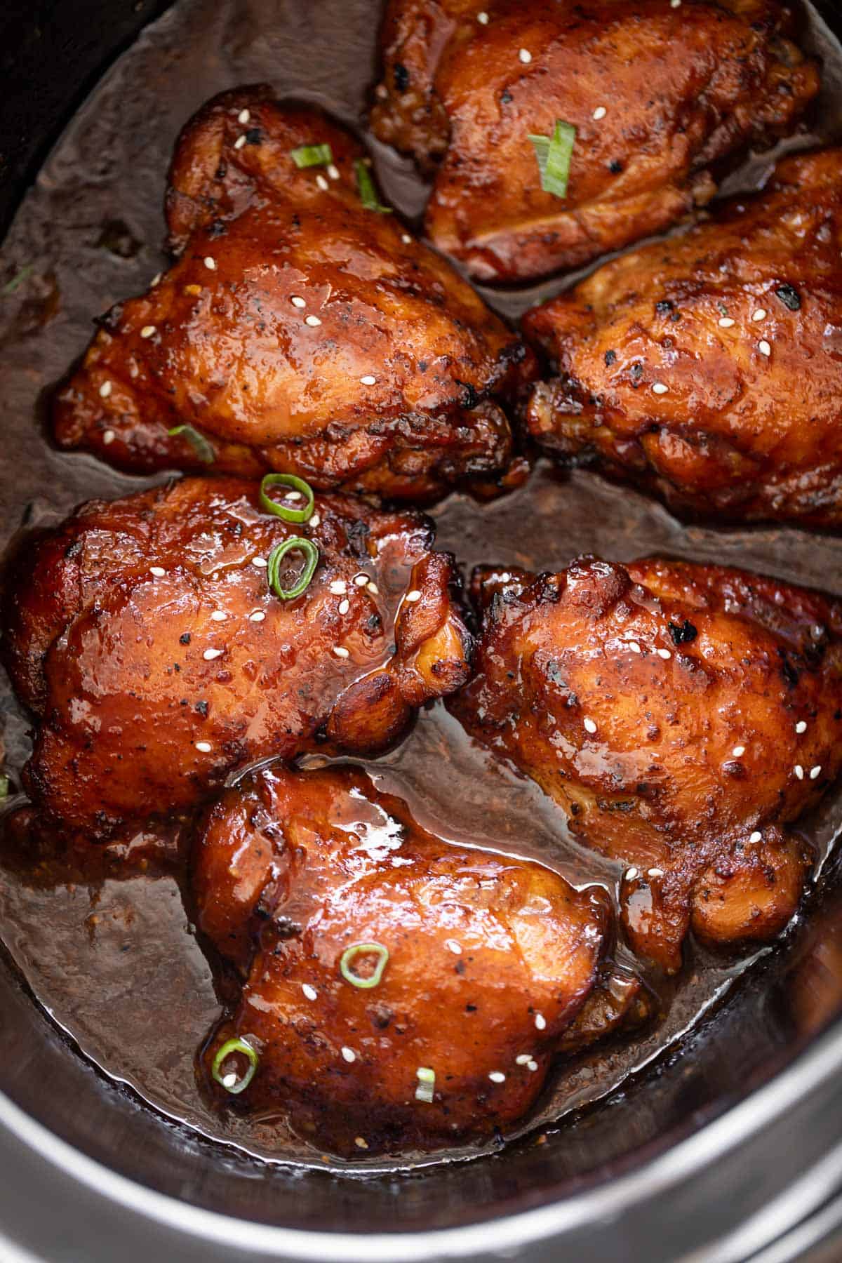 Boneless skinless chicken thighs in a black slow cooker bowl cooked in honey garlic sauce. 