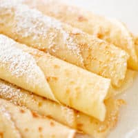 Crêpes roulées sur une assiette avec du sucre en poudre | cafedelites.com