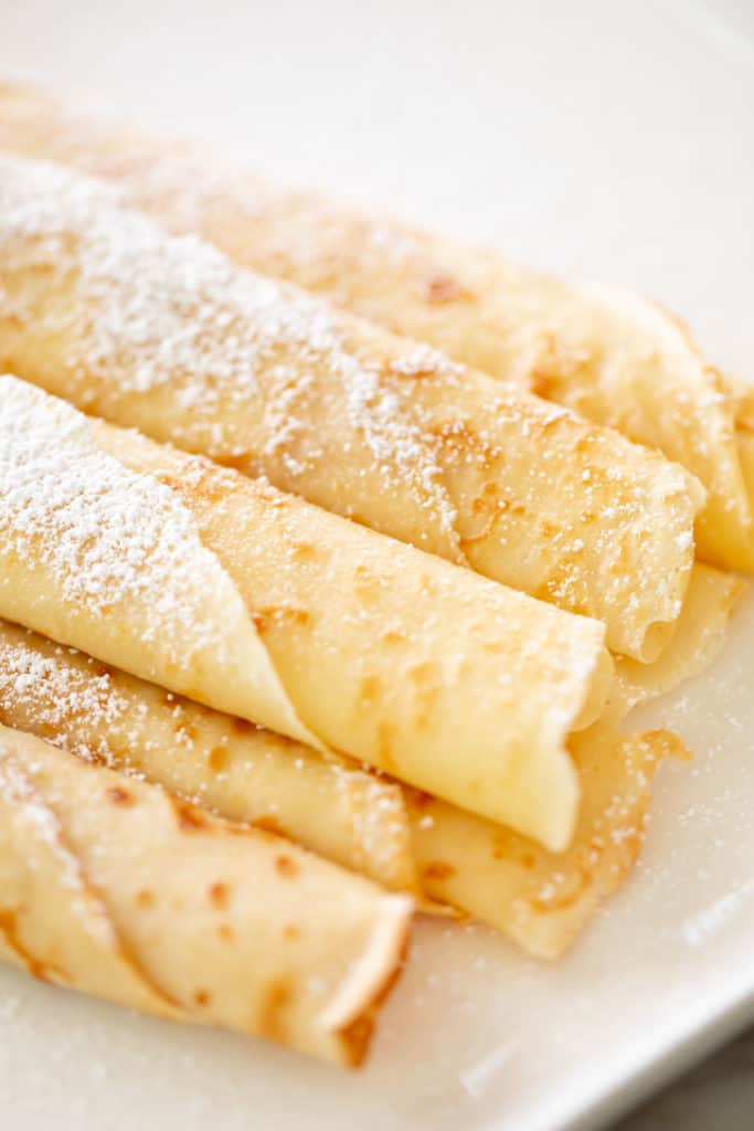 Rolled up crepes on a plate with confectioners sugar | cafedelites.com