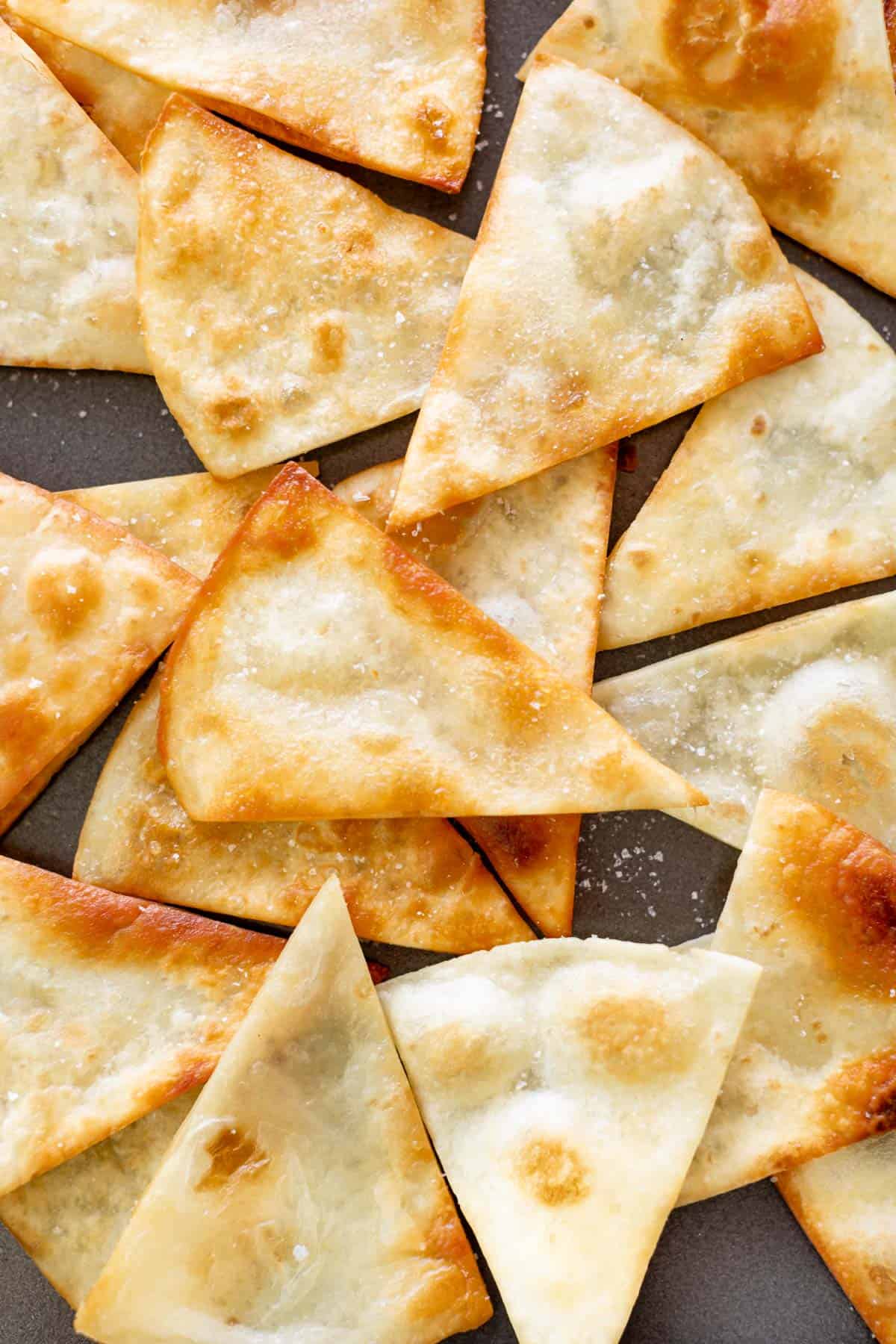 Golden tortilla chips on a plate, sprinkled with salt.