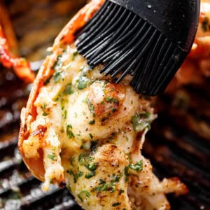 Grilled Lobster Tails brushed with melted garlic herb butter on a black grill pan.