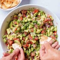 Image of the final result of the avocado salsa being scooped up with a tortilla chips by two hands.