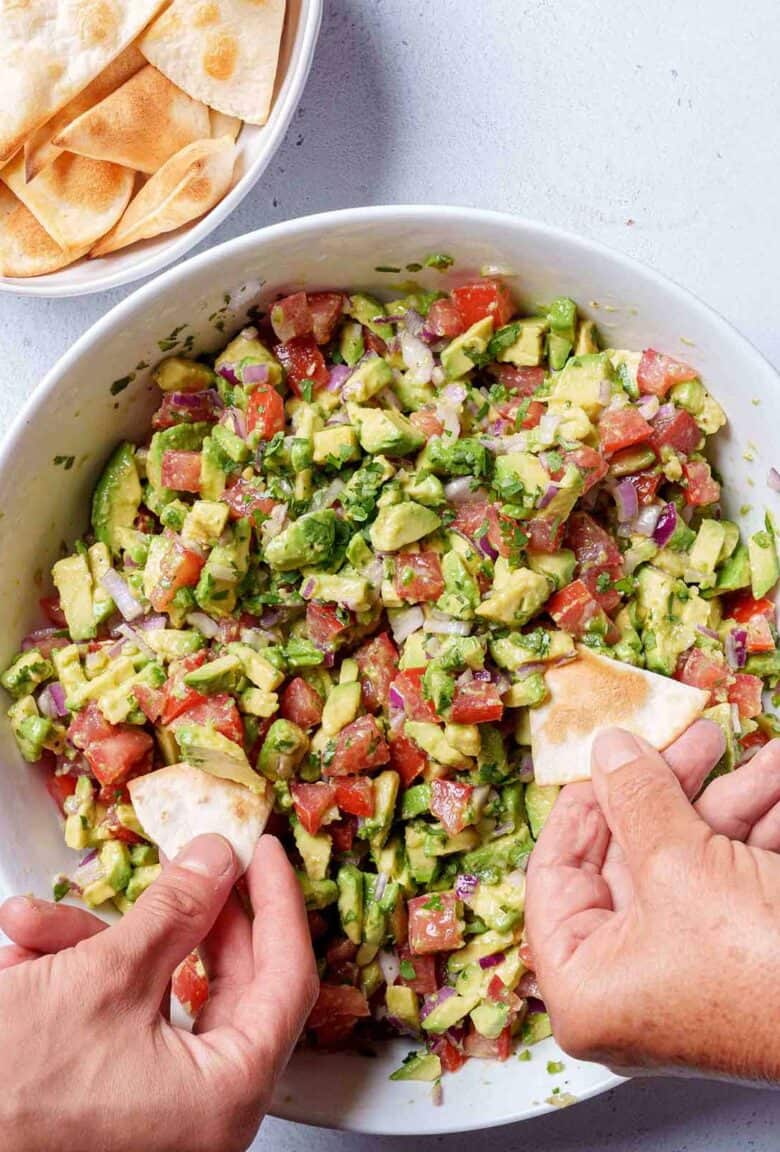 Image of the final result of the avocado salsa being scooped up with a tortilla chips by two hands.