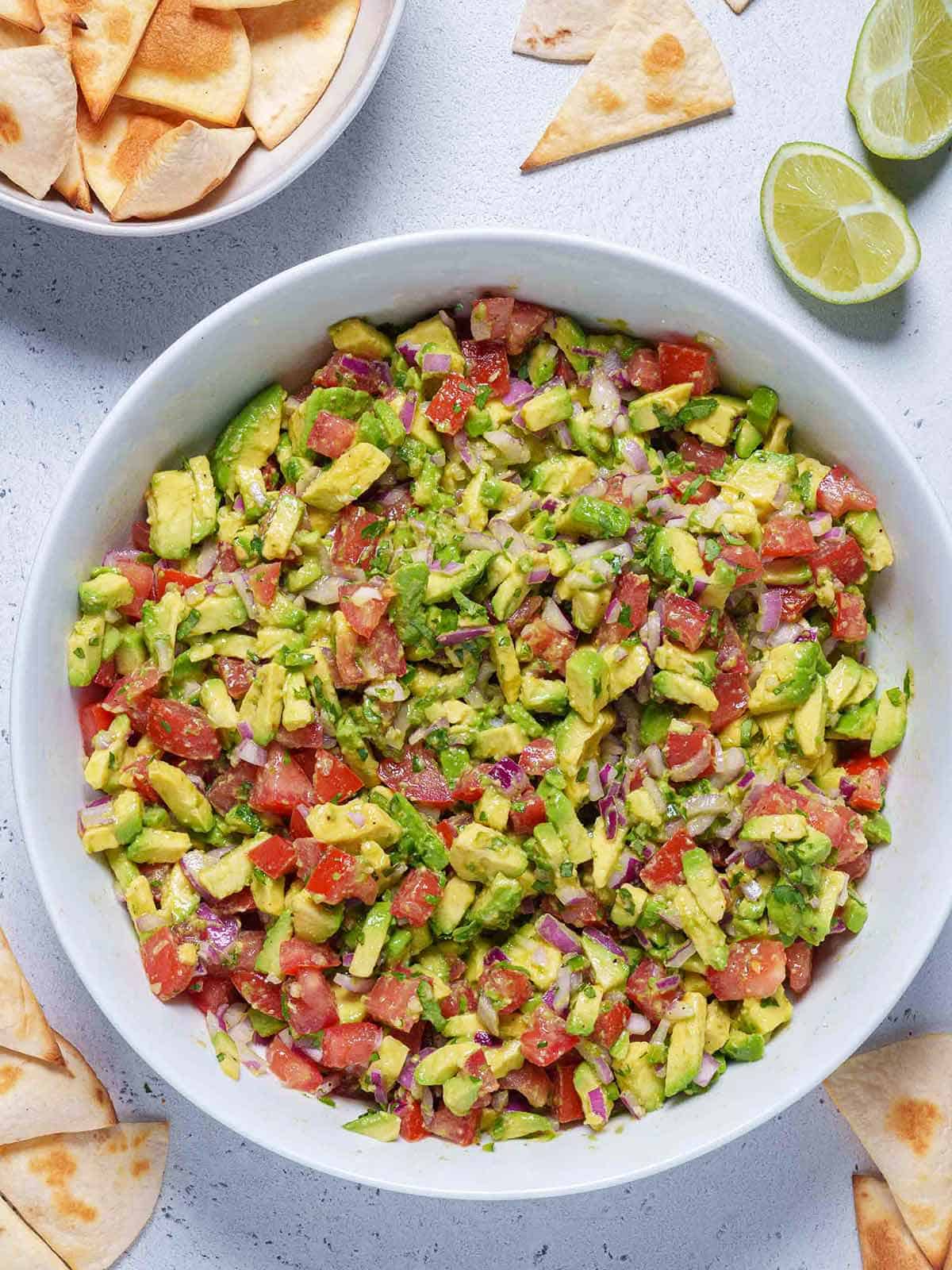 A bowl of avocado salsa made with chunky avocado bits, tomatoes, onions and a topping of cilantro and lime dressing in a white bowl.