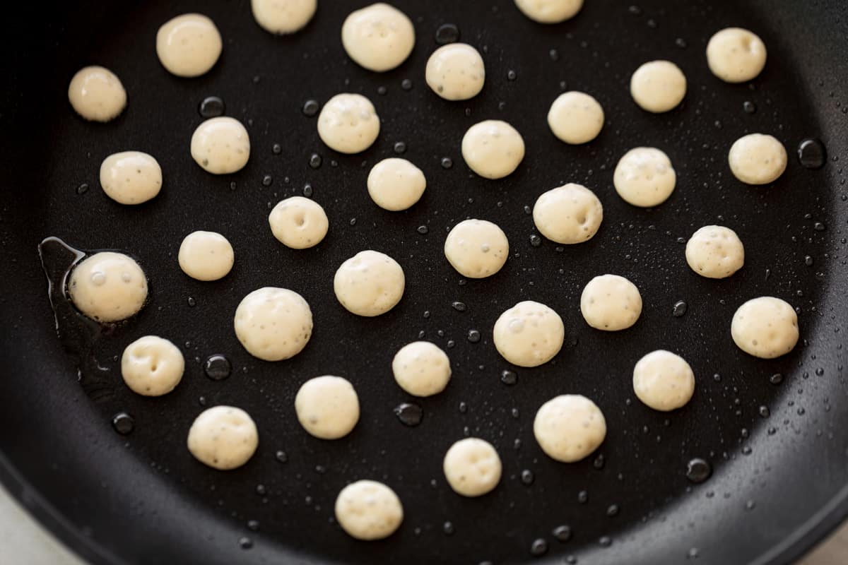 Une poêle antiadhésive noire remplie de mini crêpes prêtes à être retournées.