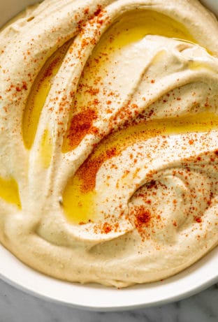 An overhead image of Hummus served in a white bowl, drizzled with olive oil and topped with a sprinkle of paprika.