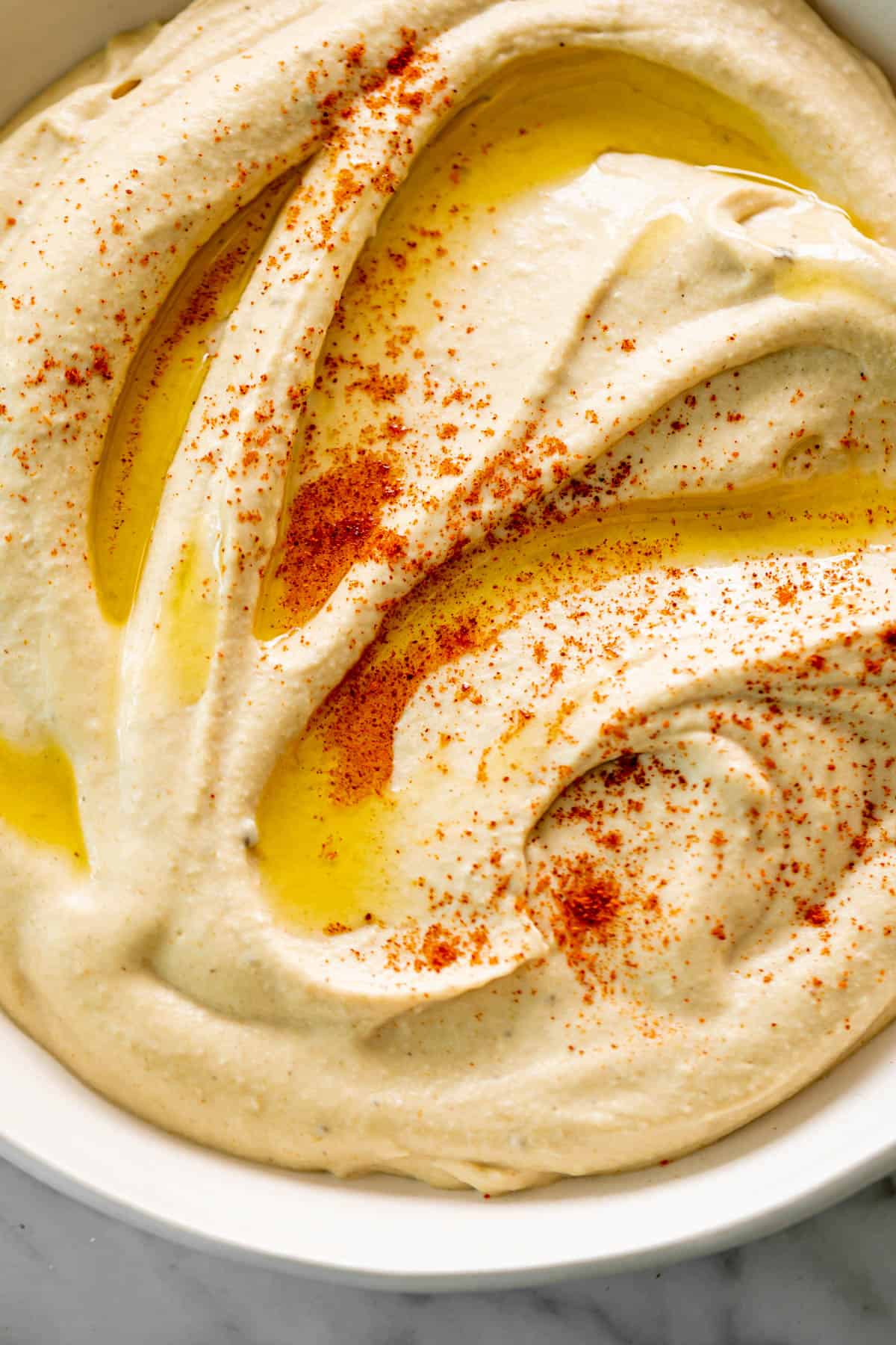 An overhead image of Hummus served in a white bowl, drizzled with olive oil and topped with a sprinkle of paprika.