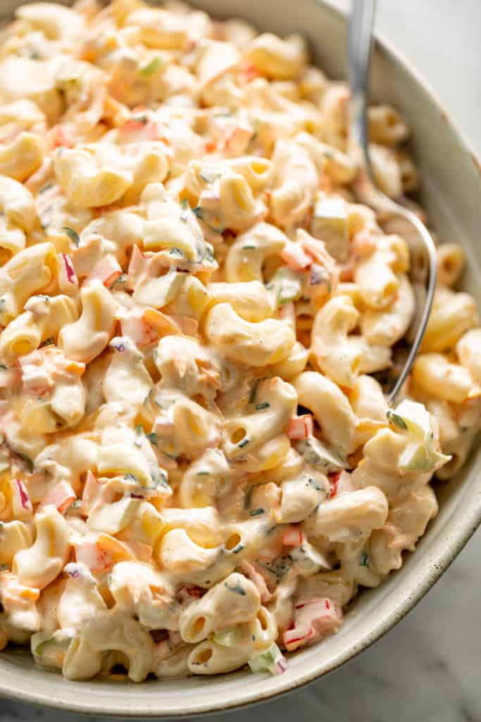 Macaroni Salad is quick to throw together and so DELICIOUS! Served in a light grey bowl on a grey linen cloth with a spoon for scooping.