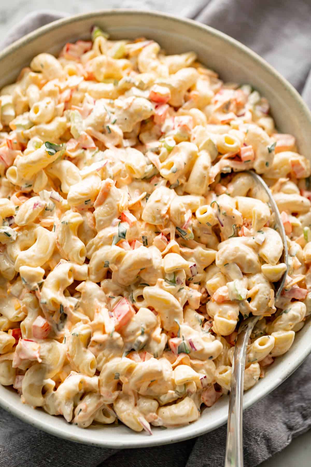 Macaroni Salad is quick to throw together and so DELICIOUS! Served in a light grey bowl on a grey linen cloth with a spoon for scooping.
