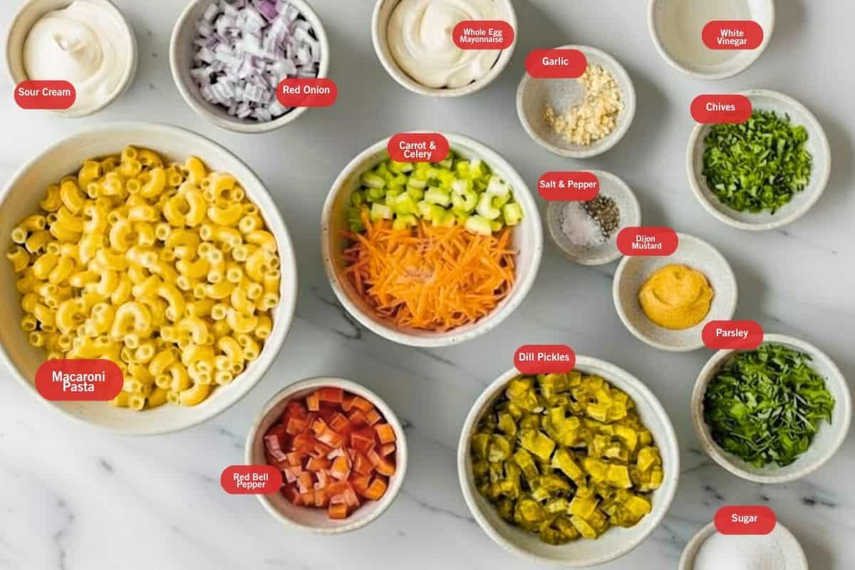 Flat lay photo of sour cream, red onion, whole egg mayonnaise, garlic, white vinegar, chives, dijon mustard, parsley, sugar, dill pickles, carrot and celery, red bell pepper, dry macaroni pasta