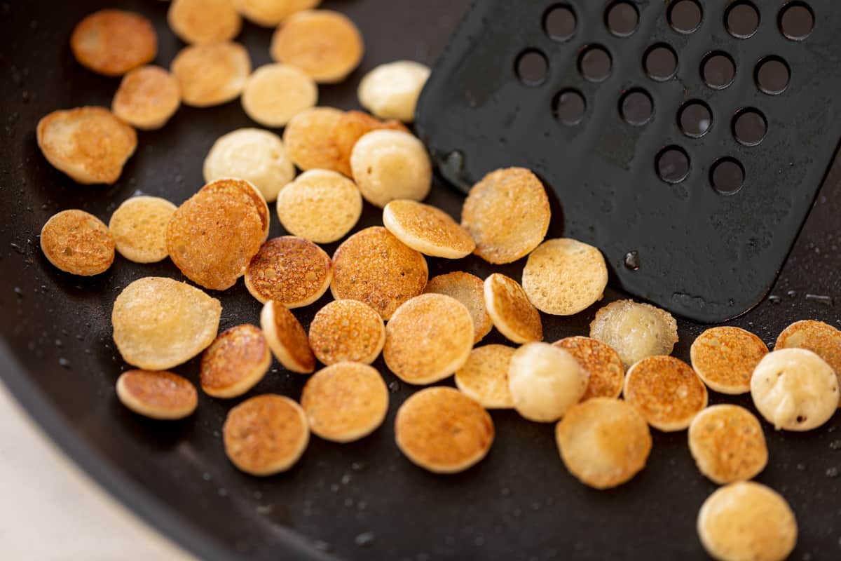 Mini pancakes cuits dans une poêle antiadhésive avec une spatule noire prête à les évider.