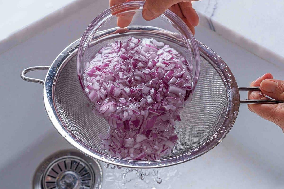 Step 1: The image shows finely chopped onions mixed with water being strained in the kitchen sink.