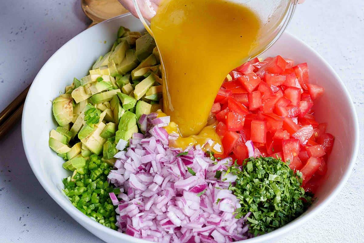 Step 4: The image shows the dressing being poured onto the chopped ingredients—avocados, tomatoes, onions, cilantro, and jalapeños—in a white bowl.