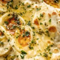 Boterig Knoflook Naanbrood van dichtbij bestreken met gesmolten knoflookboter en gegarneerd met vers gehakte koriander | cafedelites.com