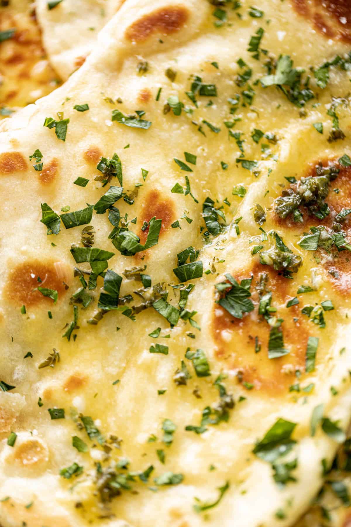 Buttery Garlic Naan Bread z bliska posmarowany roztopionym masłem czosnkowym i przyozdobiony świeżą posiekaną kolendrą | cafedelites.com