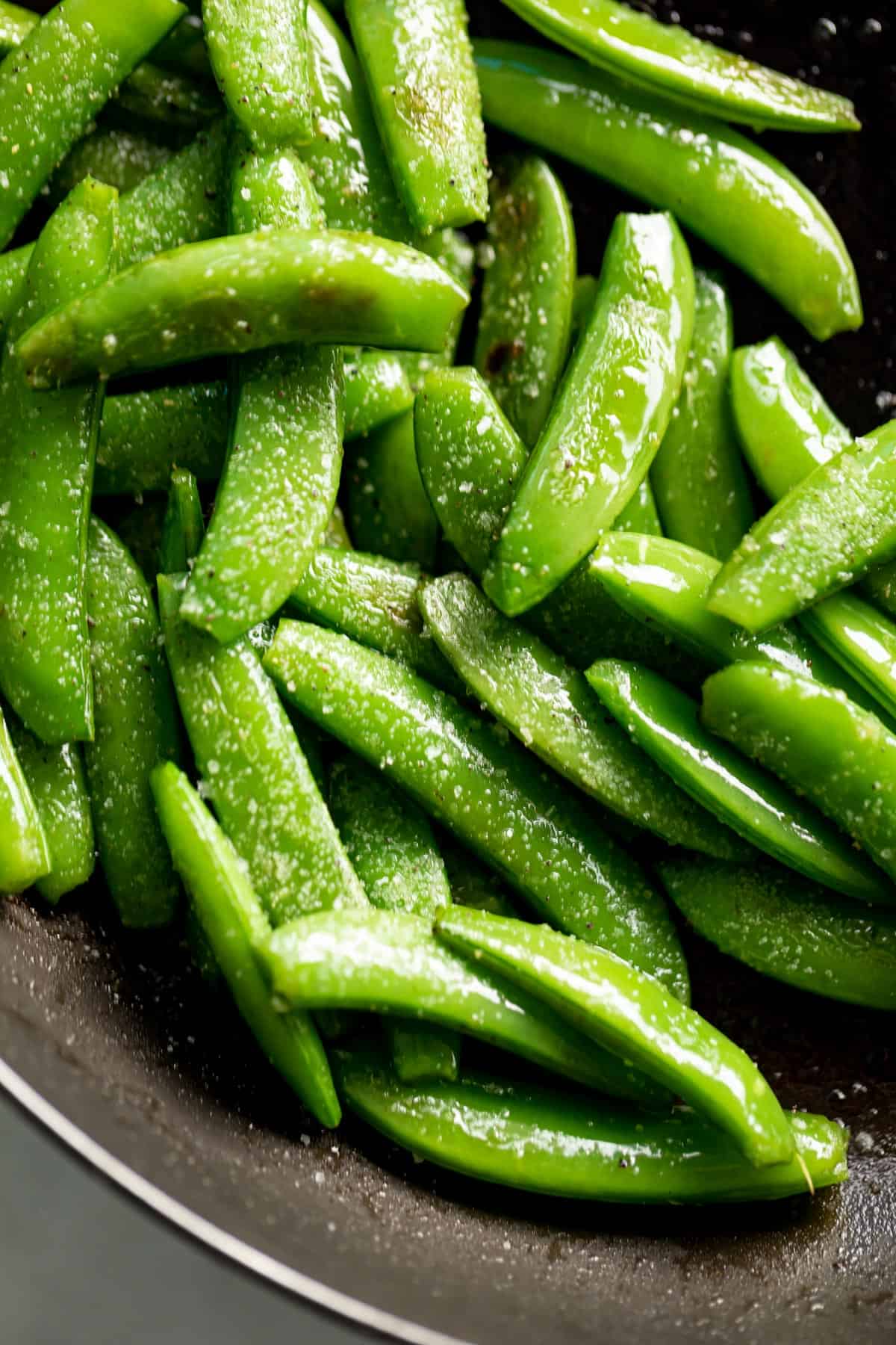 Sauteed Snap Peas in a black pan, sprinkled with coarse salt.