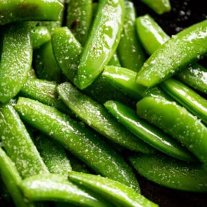 Sauteed Snap Peas in a black pan, sprinkled with coarse salt.