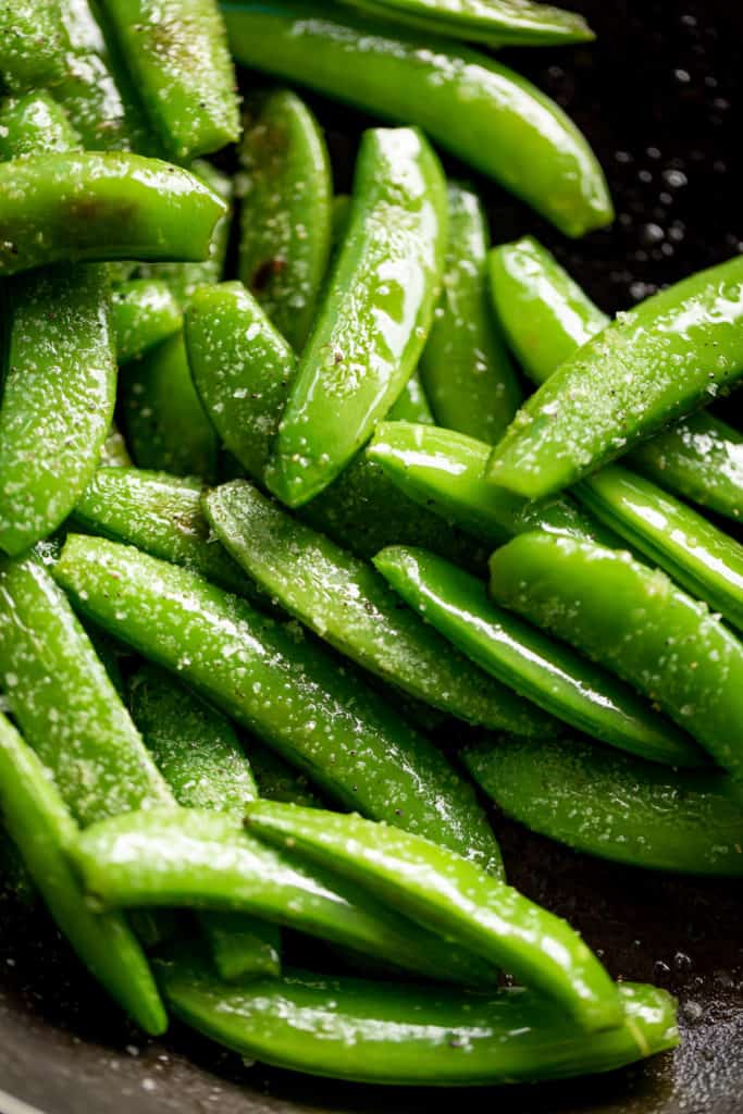 Sauteed Snap Peas in a black pan, sprinkled with coarse salt | cafedelites.com