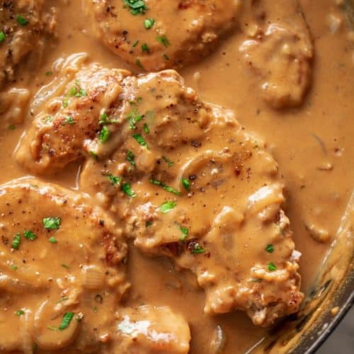 Smothered Pork Chops cooked in a black skillet garnished with fresh chopped parsley.