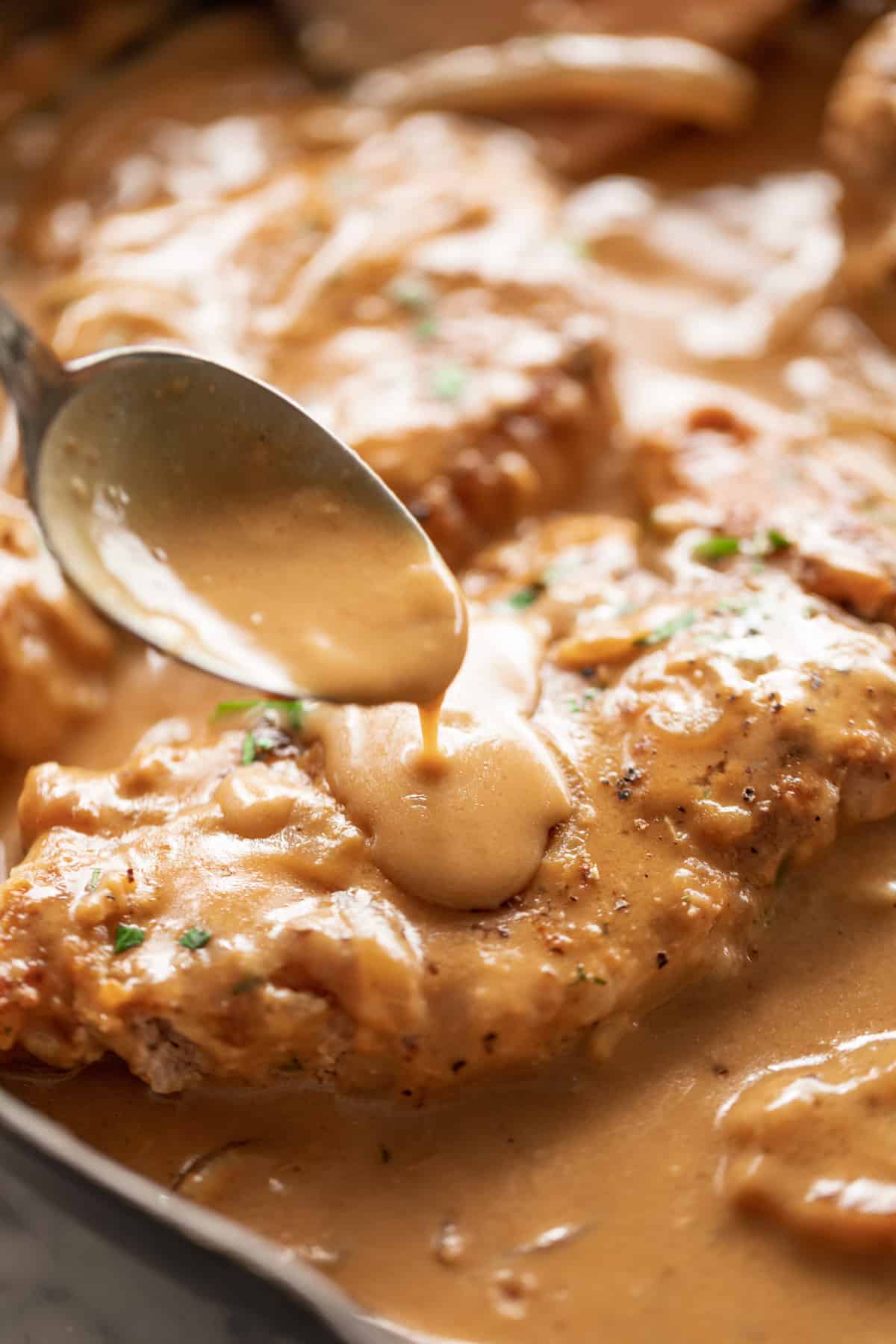 Smothered Pork Chops cooked in a rich onion gravy. Pouring gravy over one pork chop before serving