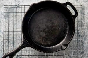 An empty black cast-iron skillet resting on a wire cooling rack over a speckled grey surface.