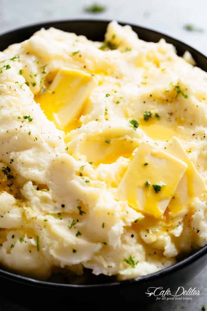 Fluffy mashed potatoes topped with green garnish and slices of melting butter in a Black bowl.