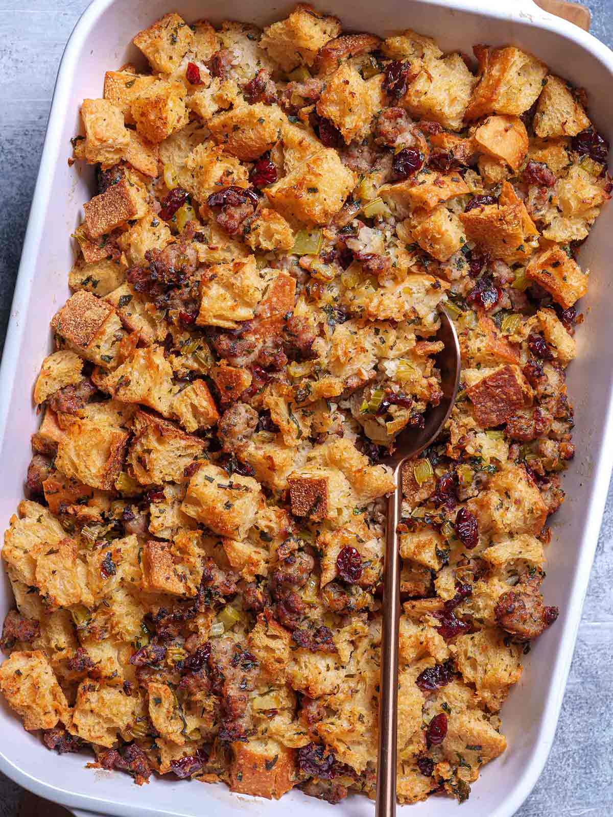 A vibrant image of the golden-finished sausage meat stuffing in a white baking tray, accompanied by a yellow spoon, is ready to be enjoyed.