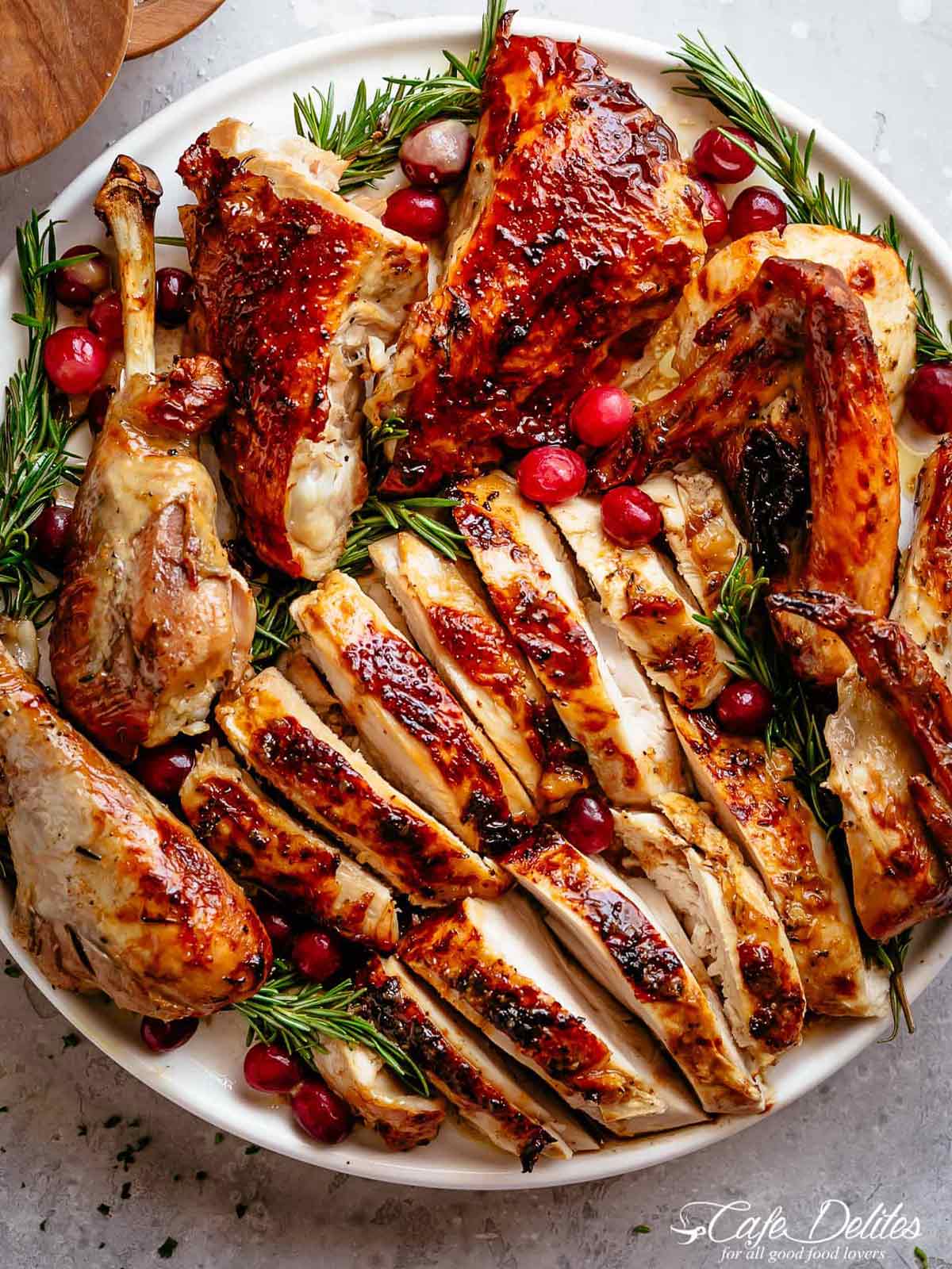 Garlic Herb Butter Roasted Turkey chopped into large slices and pieces, on a serving plate with rosemary sprigs and red cranberries strewn throughout the dish.