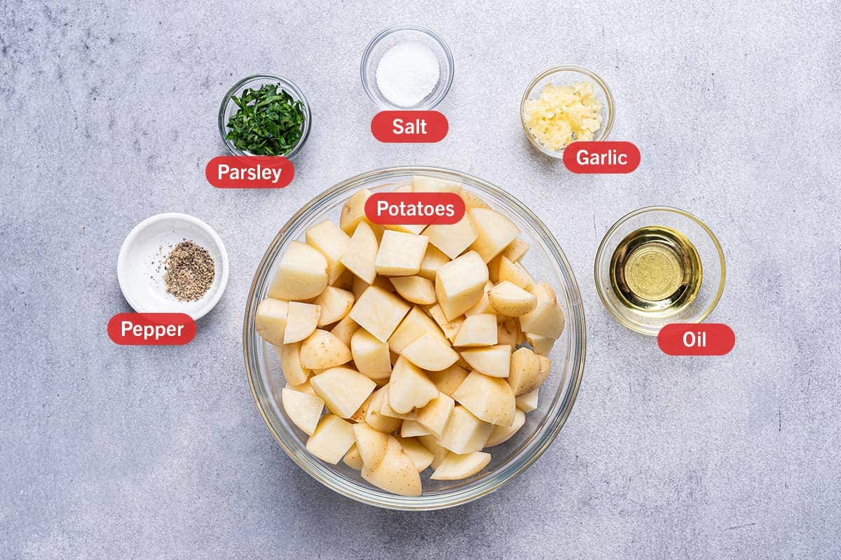image of all the ingredients needed for the preparation of garlic roasted potatoes, specifically: potatoes, pepper, parsley, salt, garlic, oil.